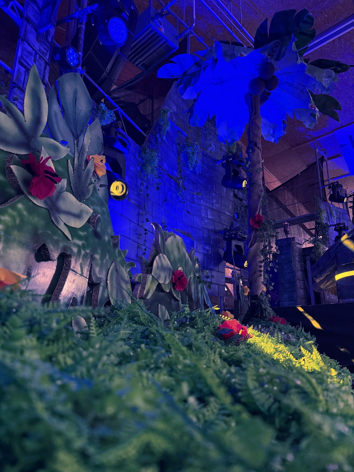 Selbstgebaute Dschungel-Deko mit Pflanzen und Blumen in der Halle, in blaues Licht getaucht
